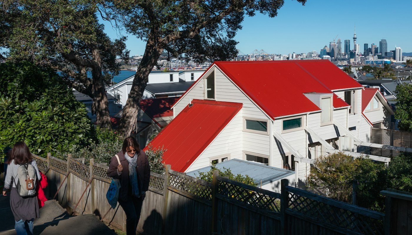 A red-roofed house above a footpath in Auckland, with the city in the distance